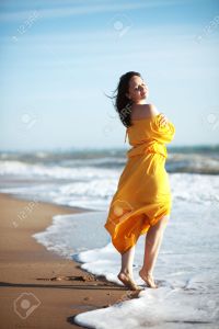 Young happy woman wearing yellow dress walking at the coastline